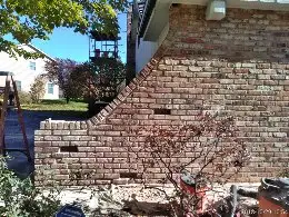 Brick wall under partial construction, showing a curved section being rebuilt with surrounding construction materials.