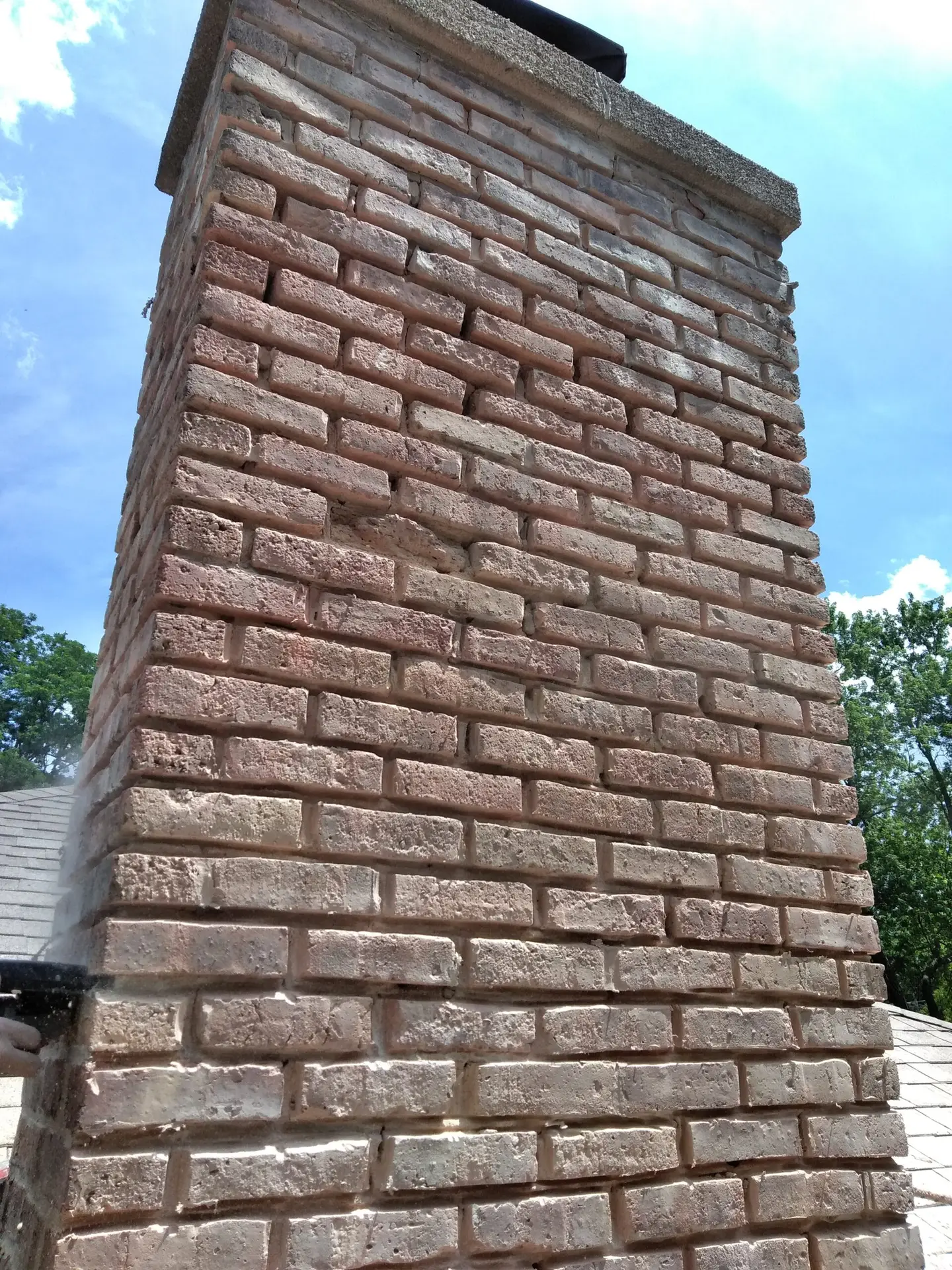 A brick chimney undergoing repair, with visible gaps between bricks, set against a clear blue sky.